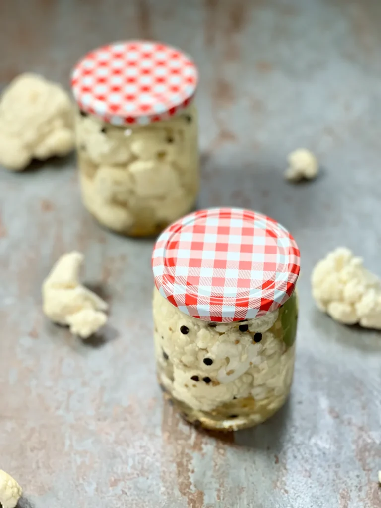 Two jars of pickled cauliflower on a grey stone plate, with florets of cauliflower around them