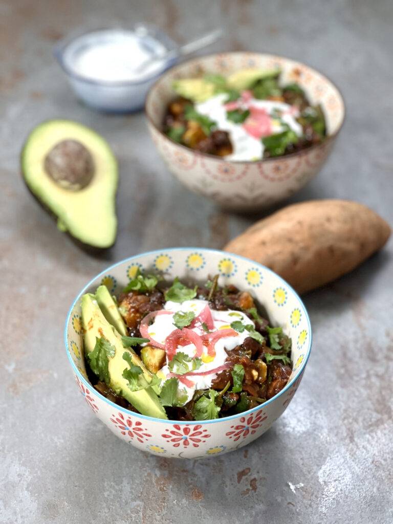 two bowls of sweet potato stew served, and a sliced avocado next to it