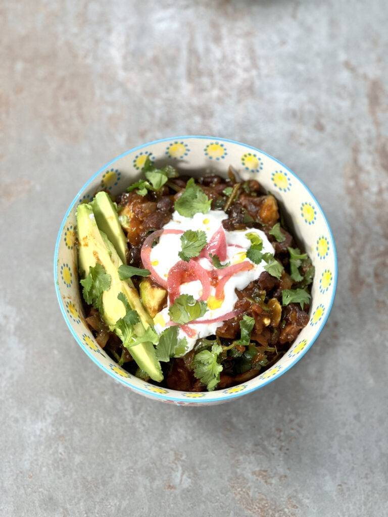 One bowl of black bean sweet potato stew nicely garnished with vegan sour cream, cilantro, avocado and pickled onions