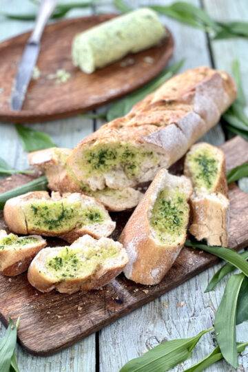 Wild garlic bread sliced on a wooden board, with wild garlic leaves around it