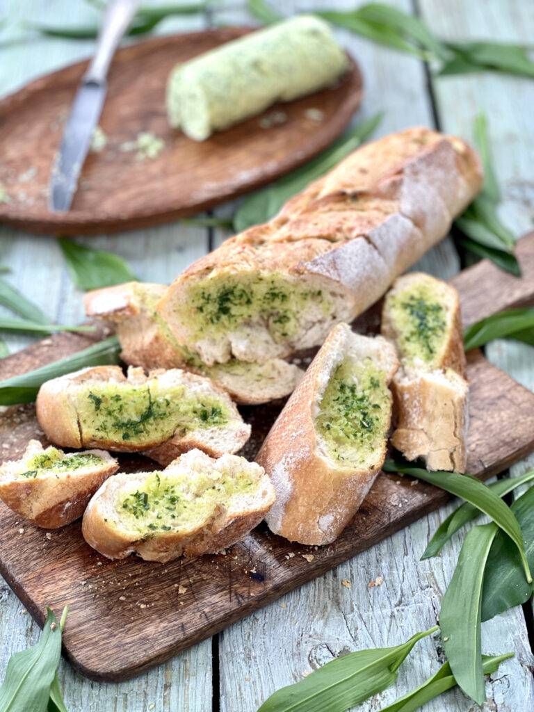 Wild garlic bread sliced on a wooden board, with wild garlic leaves around it