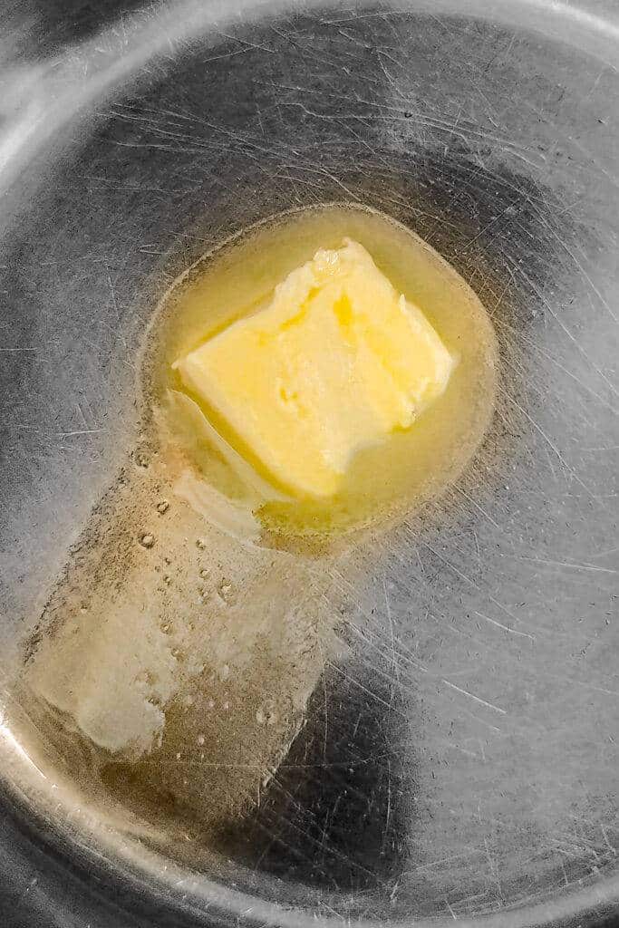 A piece of melting vegan butter can be seen in a stainless steel pot.