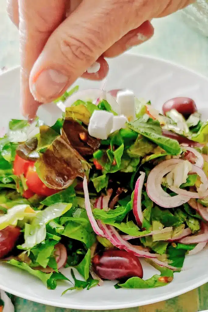A hand adds vegan feta on top of the dandelion salad.