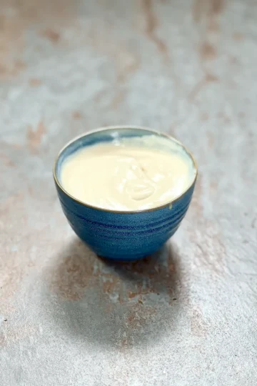 A blue ceramic bowl with creamy yogurt tahini dip on a stone plate