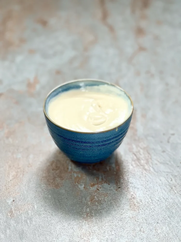 A blue ceramic bowl with creamy yogurt tahini dip on a stone plate