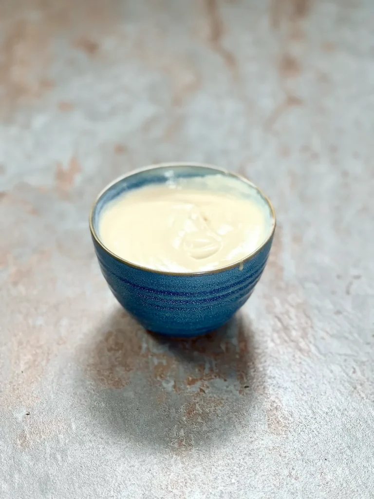 A green ceramic bowl with yogurt tahini dip on a stone surface