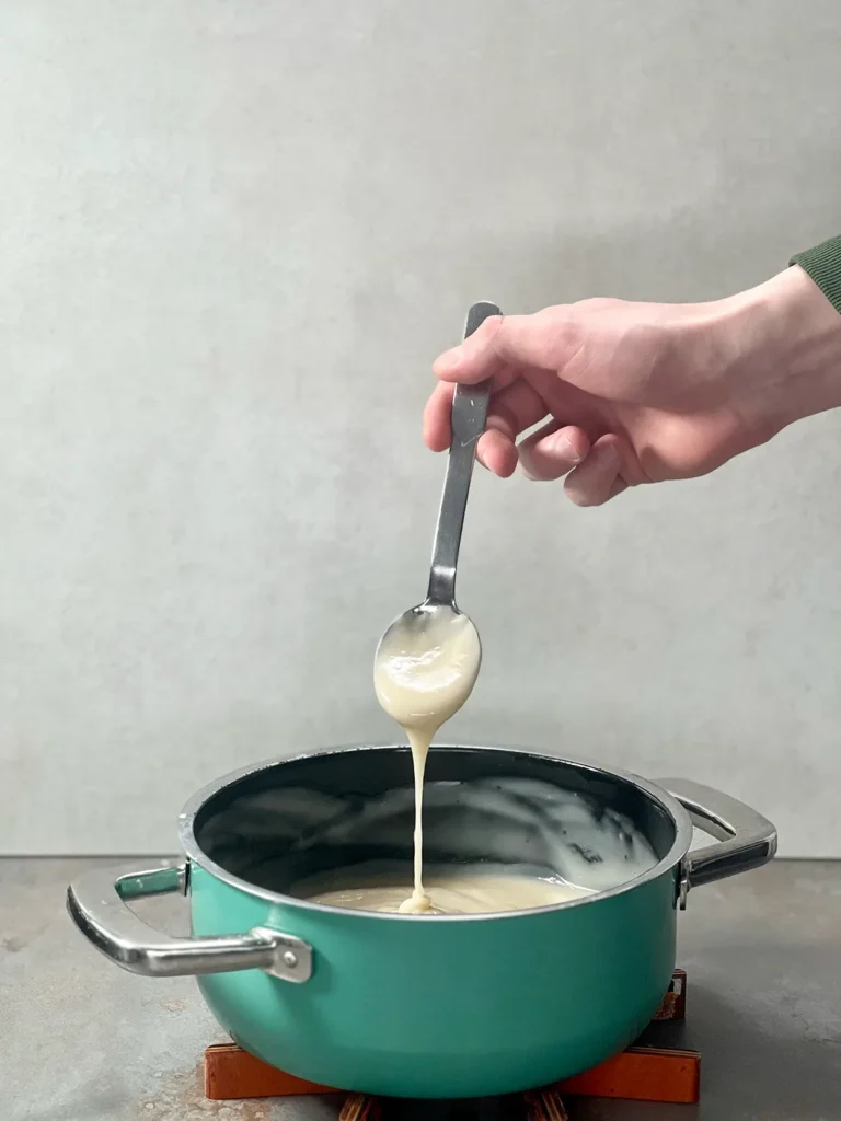 Thickened custard in a pot dripping from a silver spoon into the top.