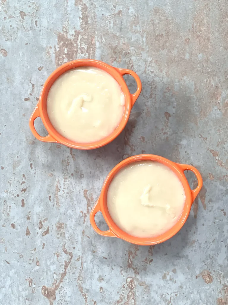 Orange ceramic ramekins filled with the vegan custard ready to go into the fridge