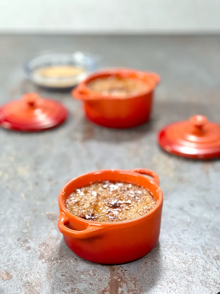 two orange ceramic ramekins with a beautiful caramel layer and a bowl of cane sugar