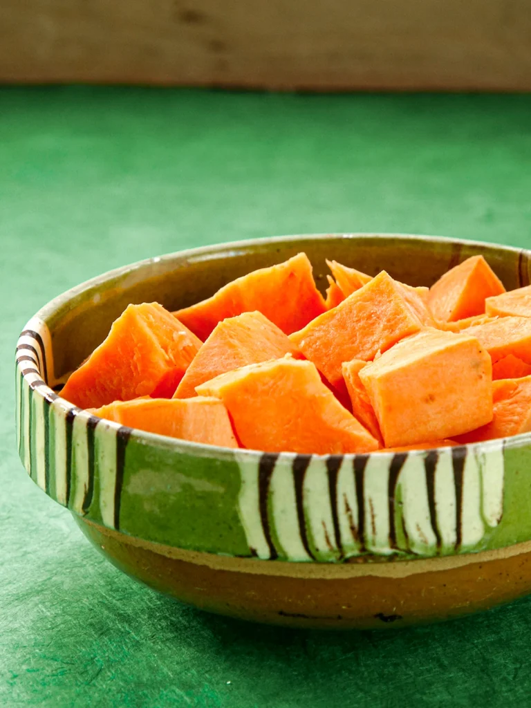 A bowl with pieces of sweet potato on a green background.