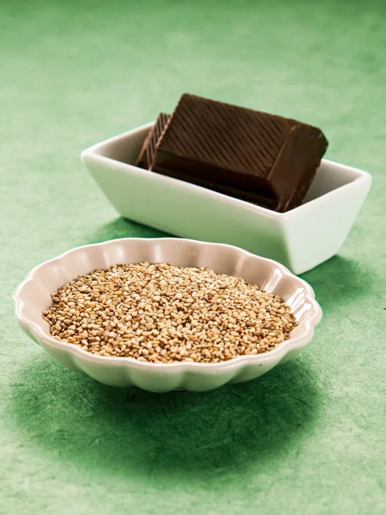 Two bowls on a green floor, one with a large chocolate bar, the other with sesame seeds.