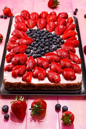 The vegan strawberry cake presented on the pink wooden base. There are some strawberries and blueberries around.