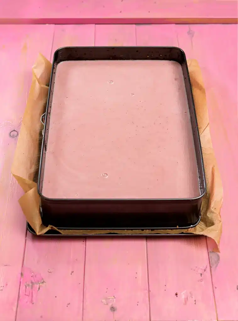Vegan Strawberry Cake with the cream layer, in the baking tin with baking paper. Stands on a pink wooden base.