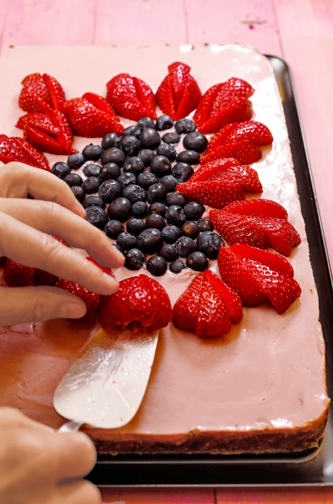 The vegan strawberry cake is being decorated with fresh fruits.