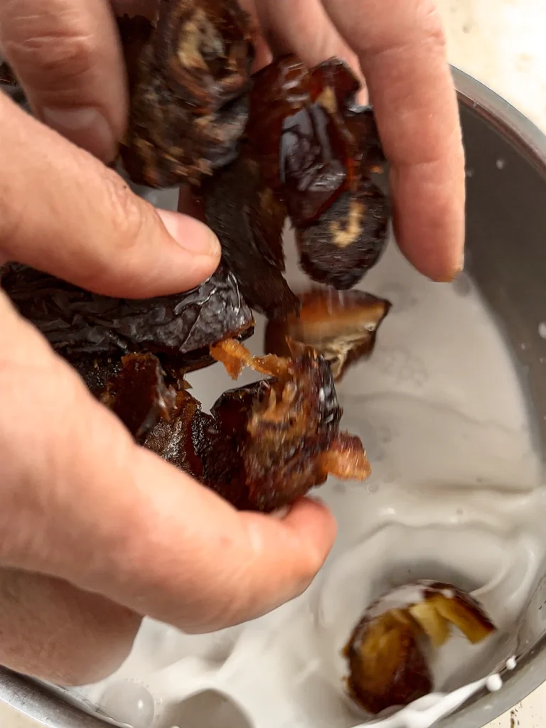 Two hands drop dates into boiling coconut milk.