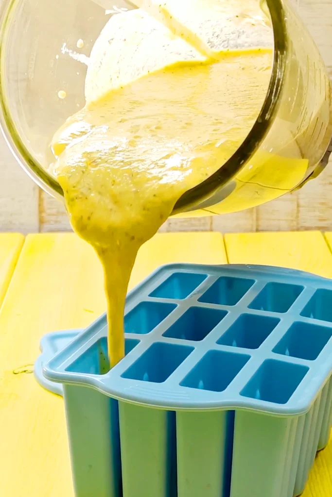 The freshly pureed mango mixture is poured from the blender container into the silicone popsicle mold.