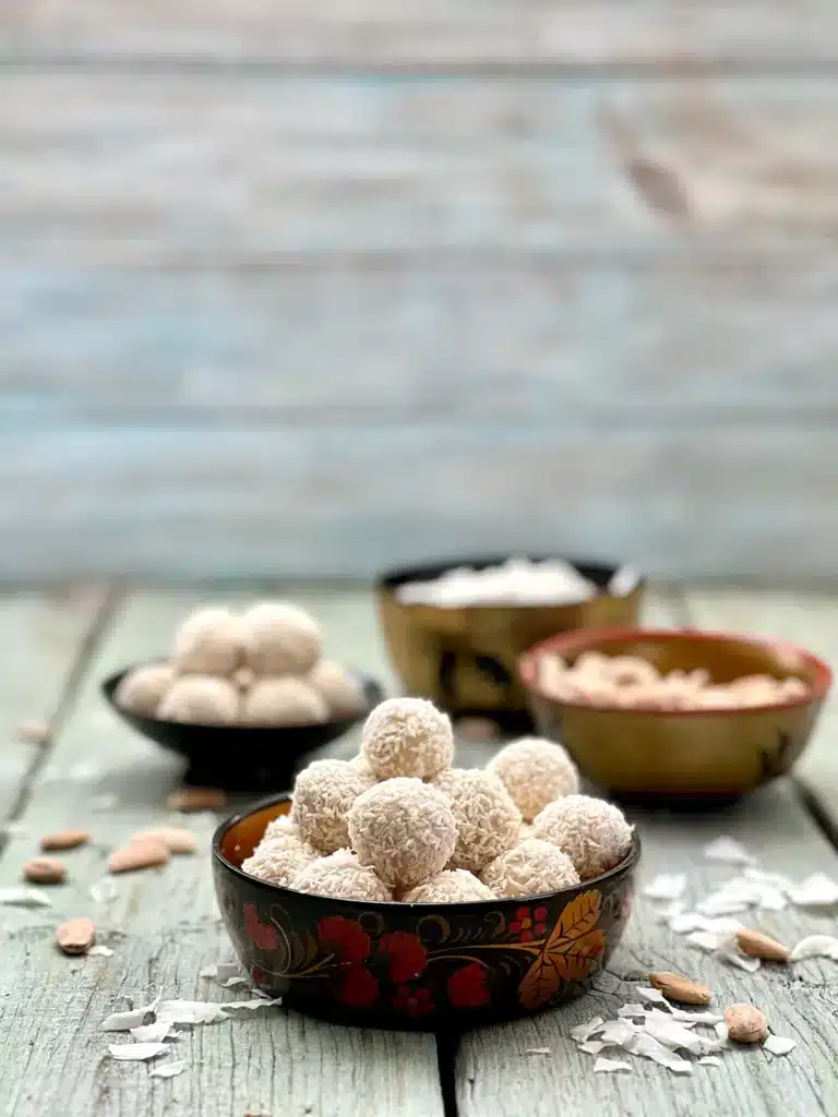 Two beautiful bowls with coconut truffles, a bowl with blanched almonds and one with shredded coconut