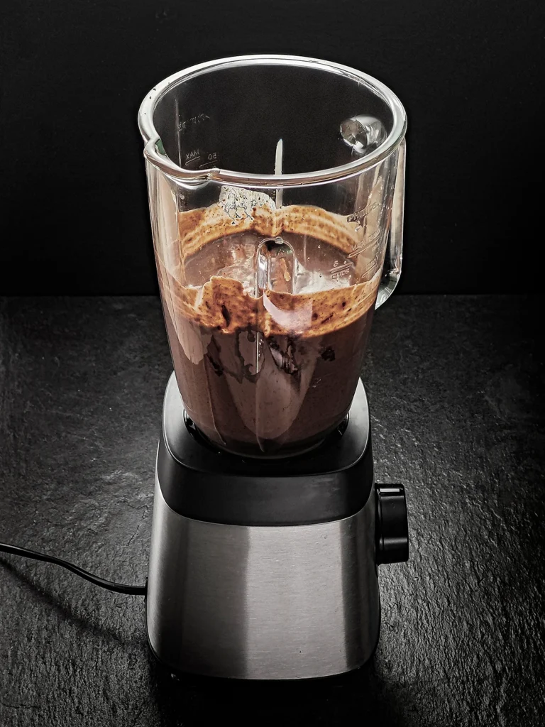 The blender on a black slate background. In its glass jar you can see the brown pureed mixture for the Halloween popsicles with sesame.