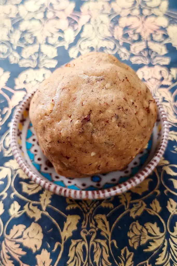 The ball of dough for crumble lies in a colorful bowl that stands on a patterned surface.