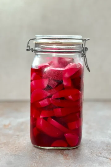 A big mason jar of Pickled Turnips on a dark stone surface