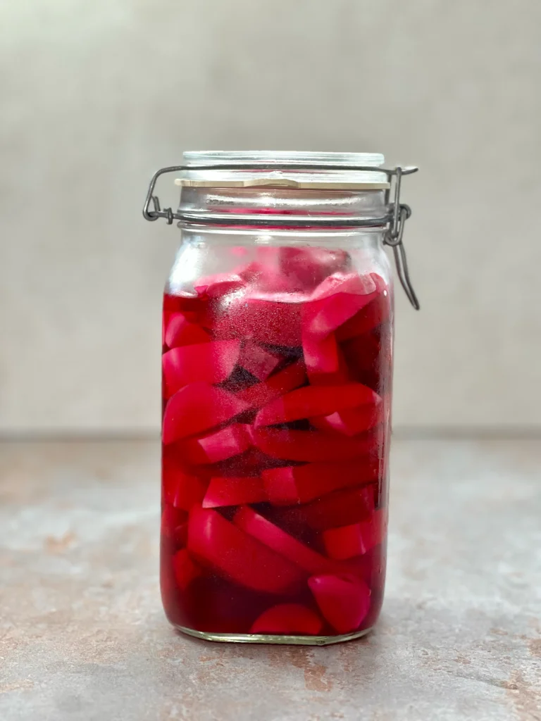 A big mason jar of Pickled Turnips on a dark stone surface