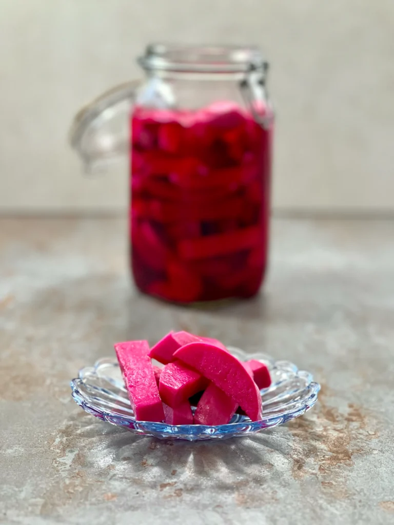 A few pieces of pickled turnip on a plate, with the mason jar standing in the background