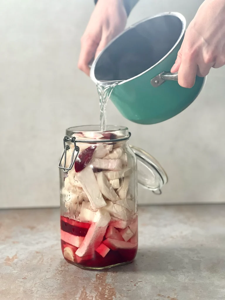 Pouring the hot brine into the mason jar, with the liquid turning a vibrant red