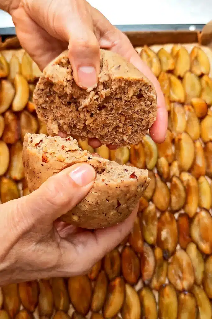 Two hands break the dough ball for the crumble over the already prepared plum cake on the baking tray.