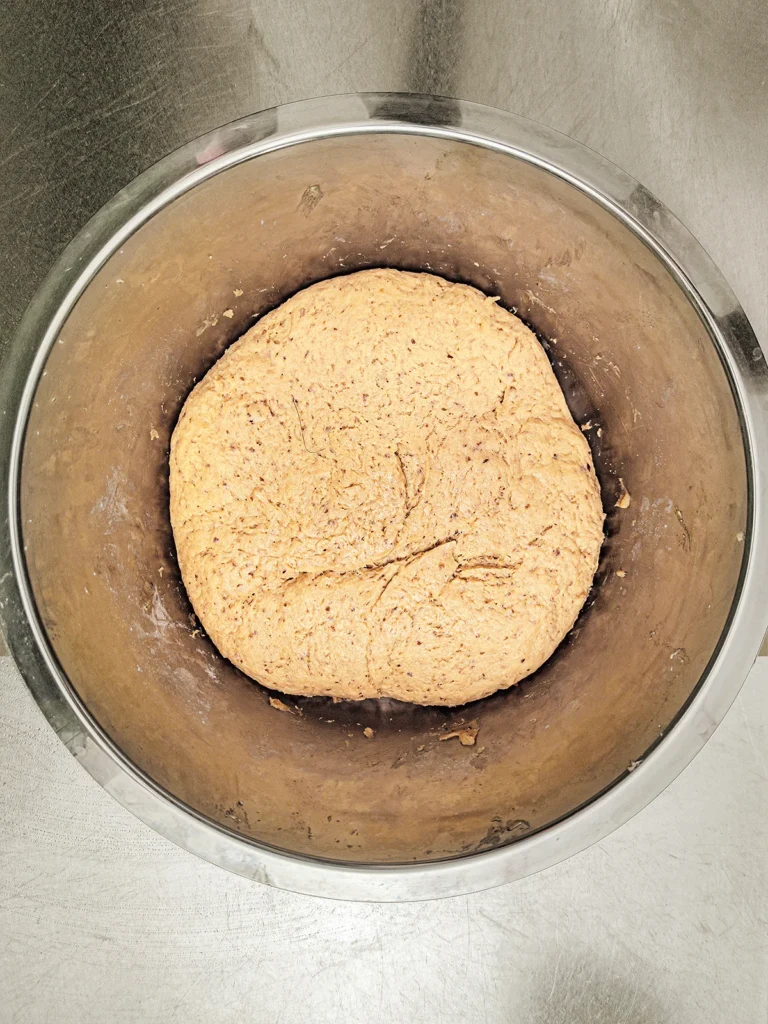 After its resting period, the risen yeast dough lies in a stainless steel bowl. The bowl stands on a stainless steel base.