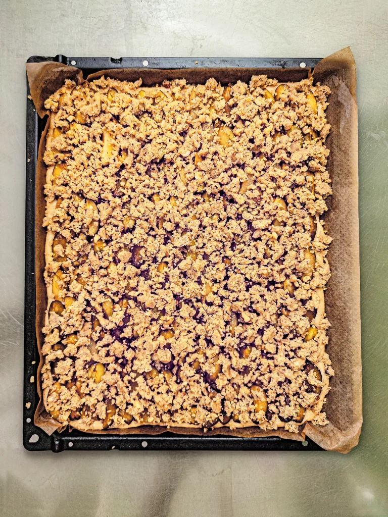 The German plum cake with hazelnut crumbles on baking paper on the oven baking tray before baking.