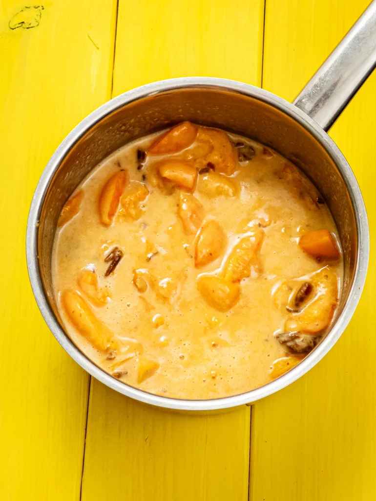 On a yellow wooden base stands a small stainless steel pot with a cooked mixture of apricots, dates and coconut milk.