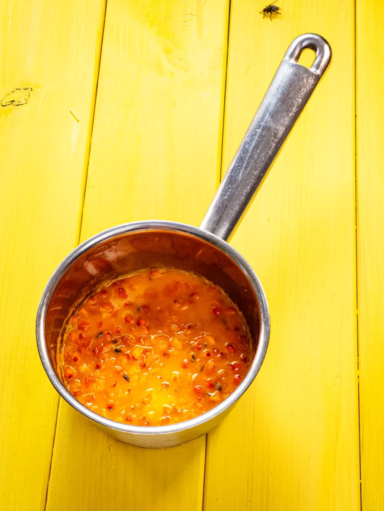 A small stainless steel pot with cooked sea buckthorn stands on a bast mat base.