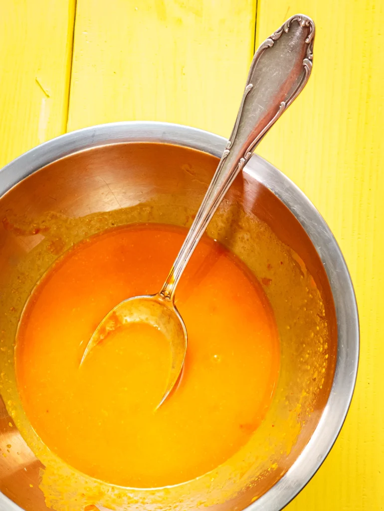 A small stainless steel bowl with a spoon and freshly sieved sea buckthorn pulp stands on a yellow wooden base.