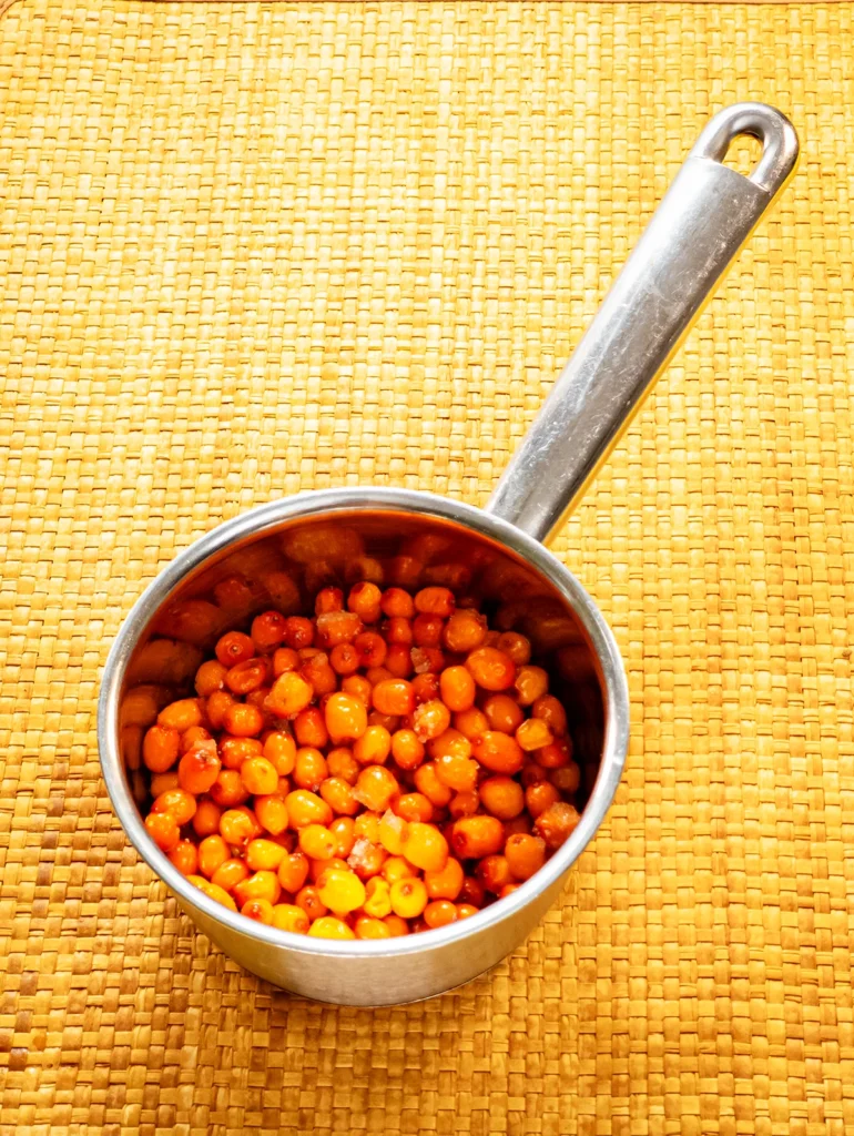 A small stainless steel pot with defrosted sea buckthorn stands on a bast mat base.