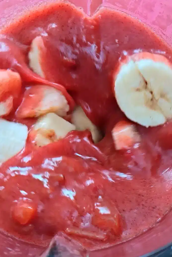 A close view into the blender with the cooked plum mixture and banana fruit slices.