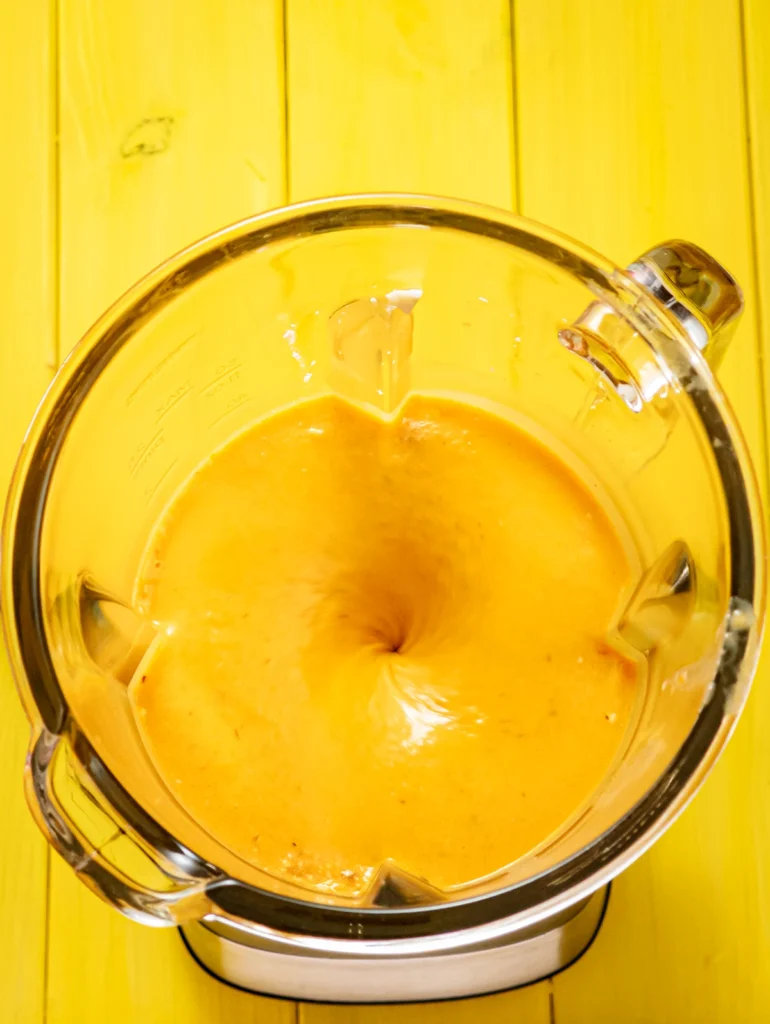 A look into the jar of the blender standing on a yellow wooden base, with the creamy mixed fruit mixture.