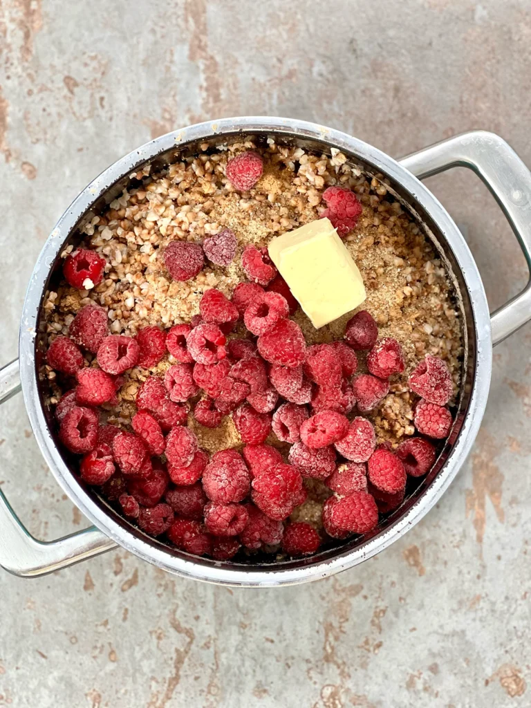 Cooked Buckwheat with frozen raspberries, sugar, spices and vegan butter substitute in a pot 