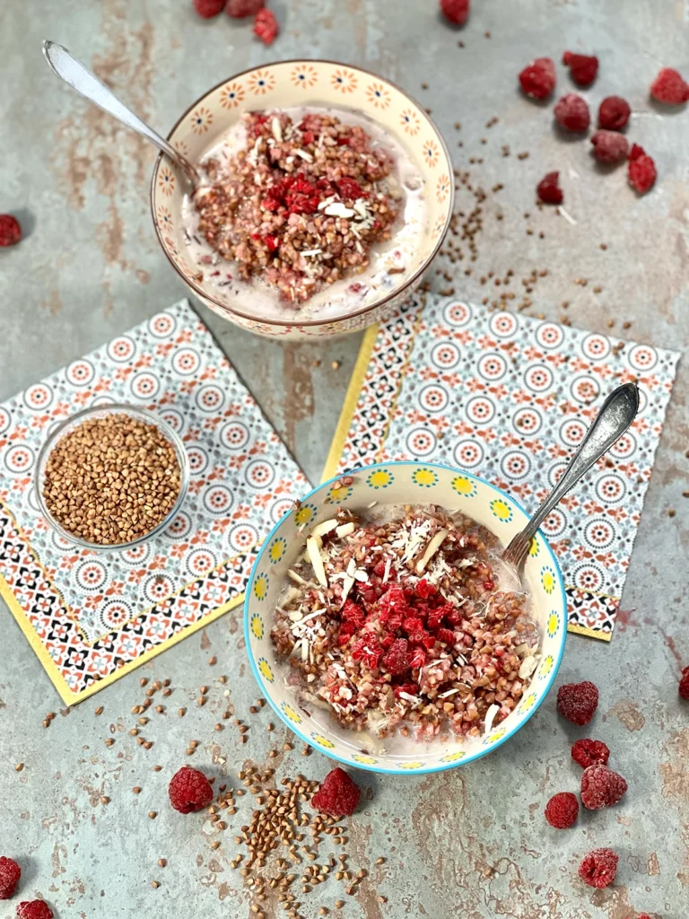 Two bowls of porridge with raspberries with silver spoons in them