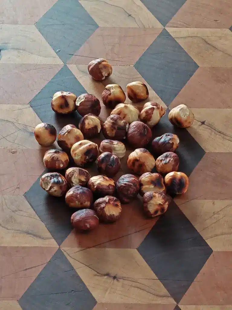 Whole roasted hazelnuts lie on a patterned wooden board.