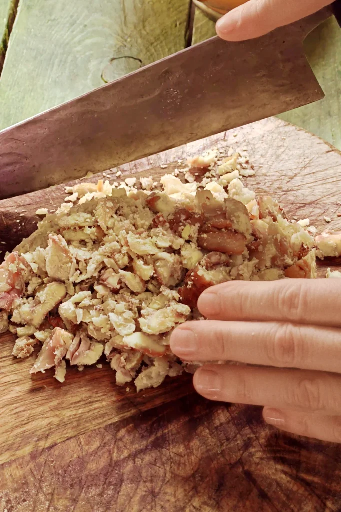 A large knife chops the pieces of chestnuts on a wooden kitchen board.