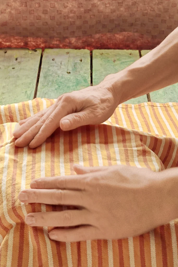 A striped kitchen towel covers the stainless steel bowl. Two hands tighten the cloth around the bowl. 