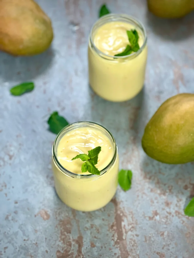 Two glasses of creamy mango lassi on a stone surface