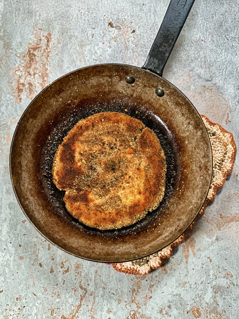 A parasol schnitzel is shallow fried in a cast iron pan