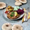 A beautiful grey plate with two parasol schitzel, braised red cabbage, cucumber salad, and potatoes. Fresh parasol mushrooms are presented around the plate.