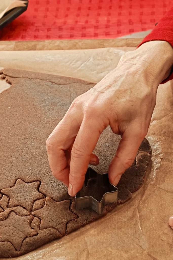 Cutting stars into the rolled out dough with a star cookie cutter. The background is a red tablecloth.