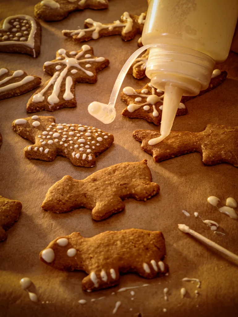 The icing is in a sauce bottle with a plastic piping nozzle. Gingerbread cookies are being decorated on baking paper.