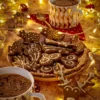 Festive gingerbread cookies decorated with vegan icing, served on a holiday-themed plate alongside two cups of hot cocoa, surrounded by warm fairy lights and Christmas ornaments.