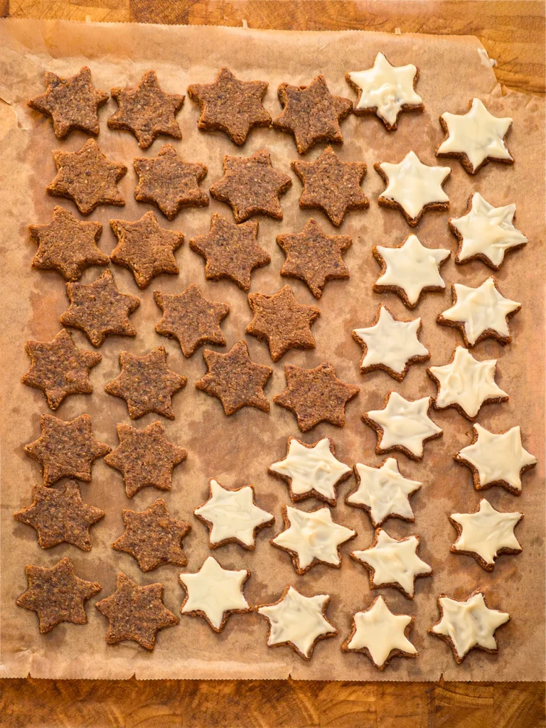 All the Cinnamon Star Cookies are lying on on baking paper.Half of the cinnamon star cookies are glazed white, with vegan white chocolate coating.