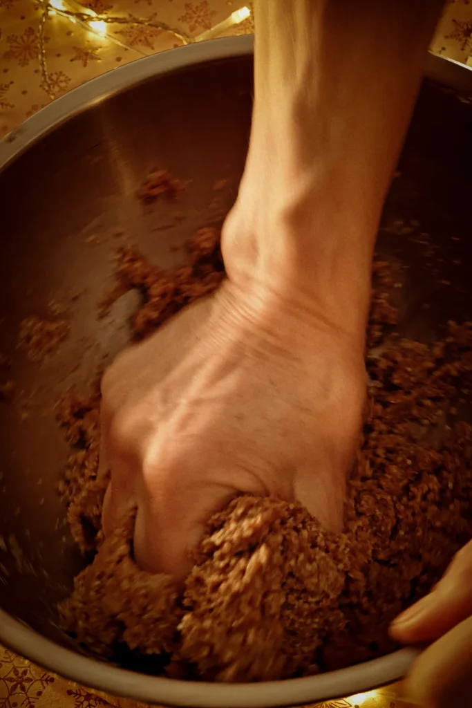 A hand kneads the gingerbread cookie dough in a stainless steel bowl.