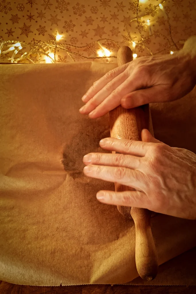 Roll out the dough with a rolling pin between baking paper. A string of lights glows in the background.